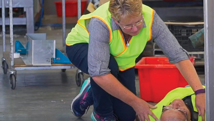 Woman kneeling next to unconcious man - both in high vis gear.